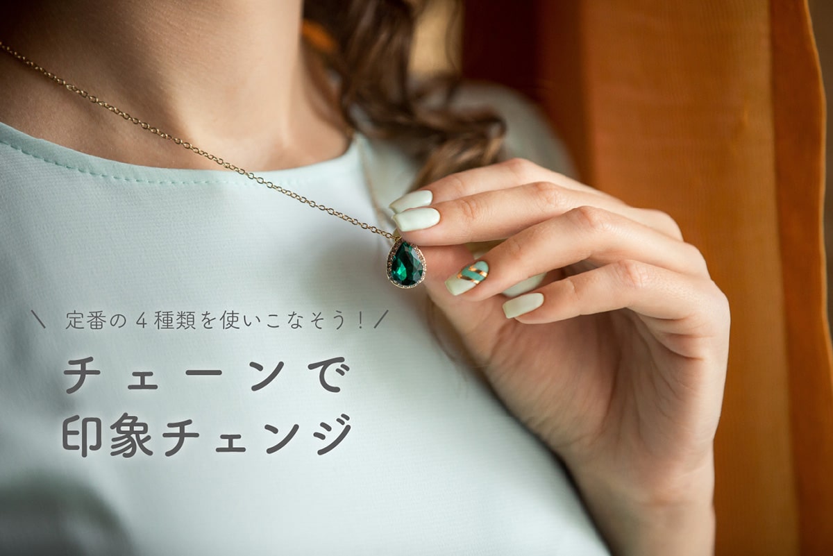 緑色の宝石のついたネックレスに触る女性の手